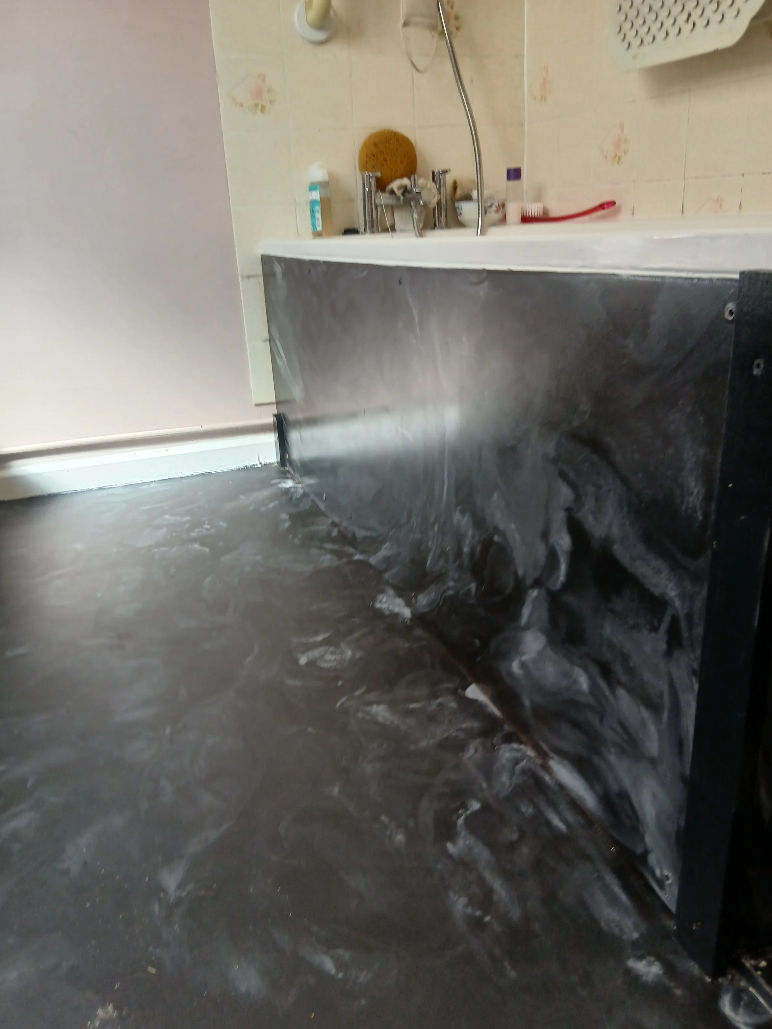 Bathroom with a black marble floor, wall tiles, a bathtub, and toiletries on the edge of the tub.