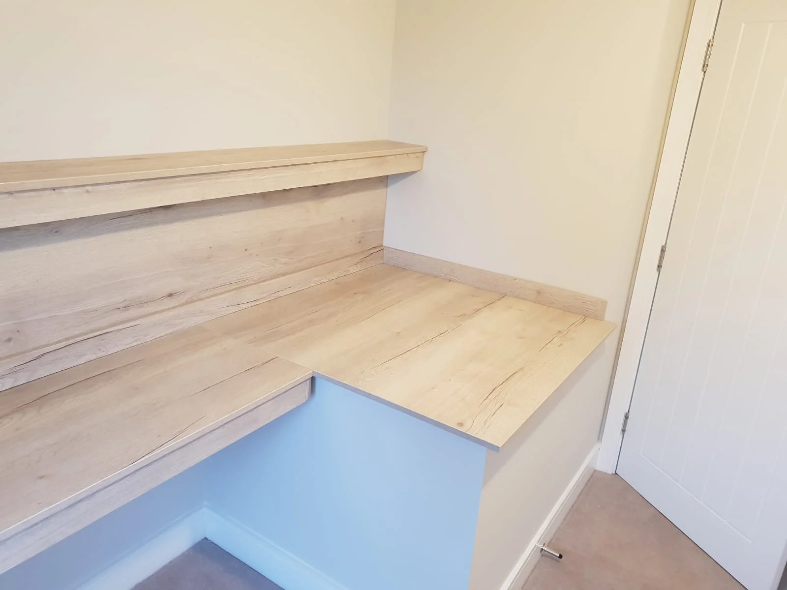 A corner of a room with a wooden desk and a built-in wooden shelf on the wall.