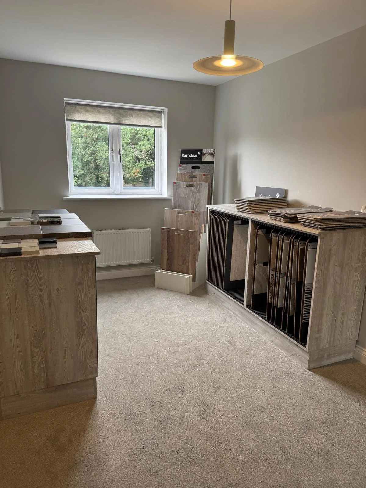 Interior of a showroom displaying laminate and flooring samples with a window and ceiling light.
