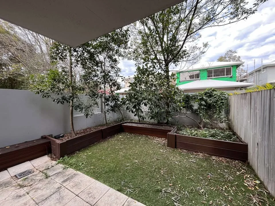 Backyard with raised garden beds, a small patch of grass, and trees, with neighboring houses visible in the background.