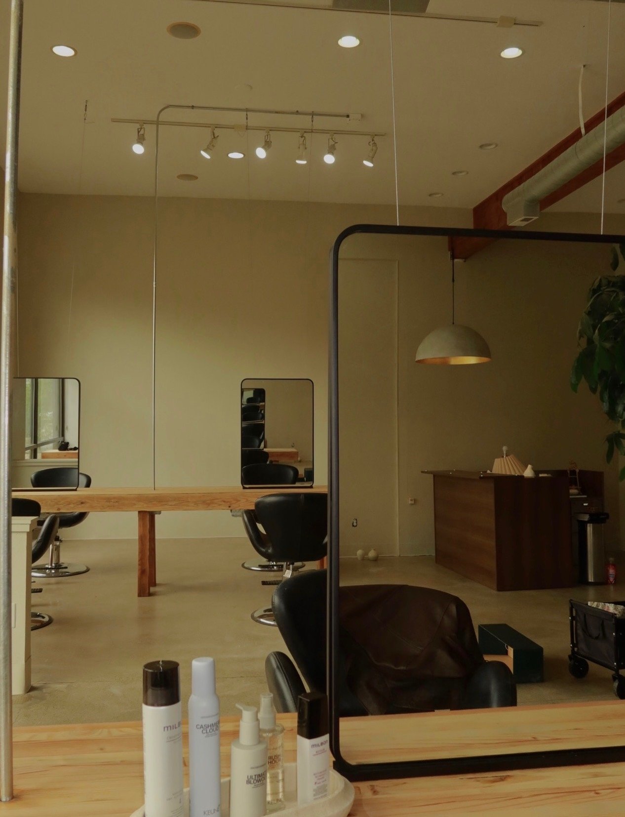Interior of a hair salon featuring styling chairs, mirrors, a wooden reception desk, pendant lighting, and skincare bottles on a counter.