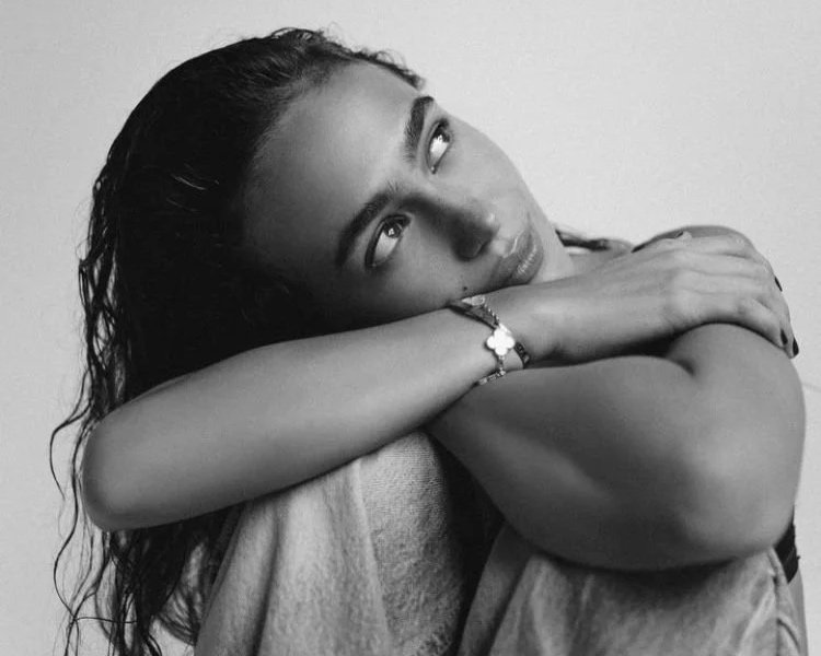 A young woman with wet hair resting her head on her crossed arms, looking up thoughtfully.