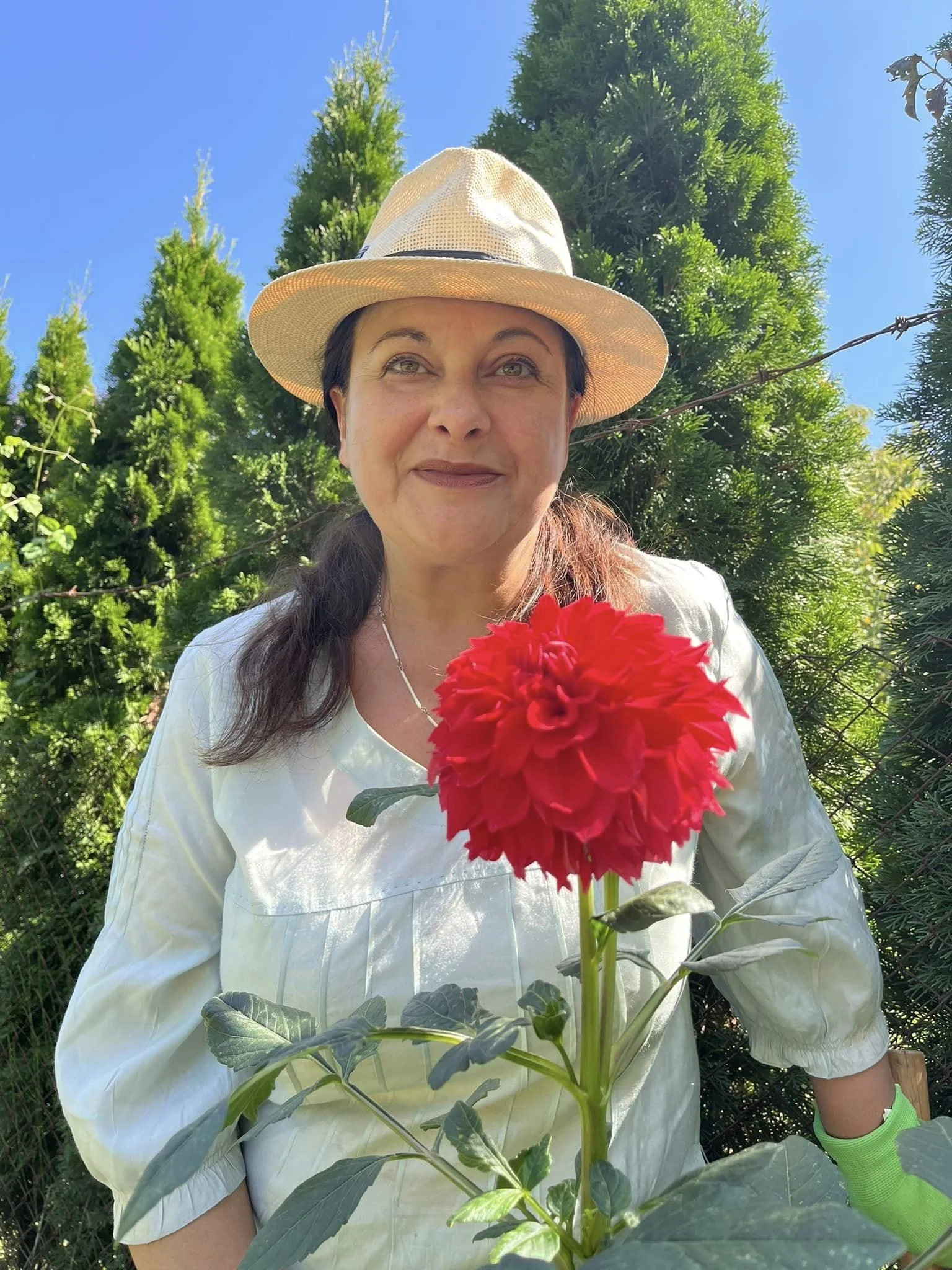 Жена с бяла рокля, сламена шапка, в градина и червено цвете