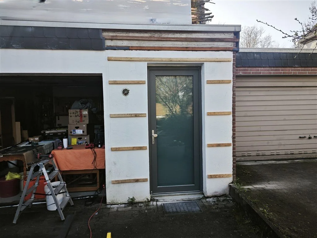 Vorbereitung einer Fassadenverkleidung aus Holz: Ein Garagennebeneingang in Bielefeld mit einer neuen anthrazitfarbenen Glastür und horizontaler Montage-Lattung auf weißem Putz.