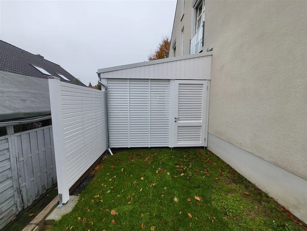 Rückansicht eines weißen Holz-Carports (endbehandelt), mit Fichte Rhombusprofil-Sichtschutzwand zum Garten und abschließbarer Durchgangstür.