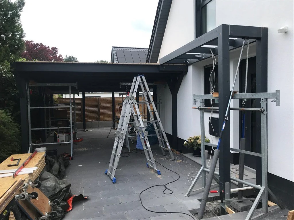 Moderner Carport direkt am Haus mit integrierter Haustürüberdachung; Konstruktion aus Fichte-Leimholzbindern in Anthrazit.