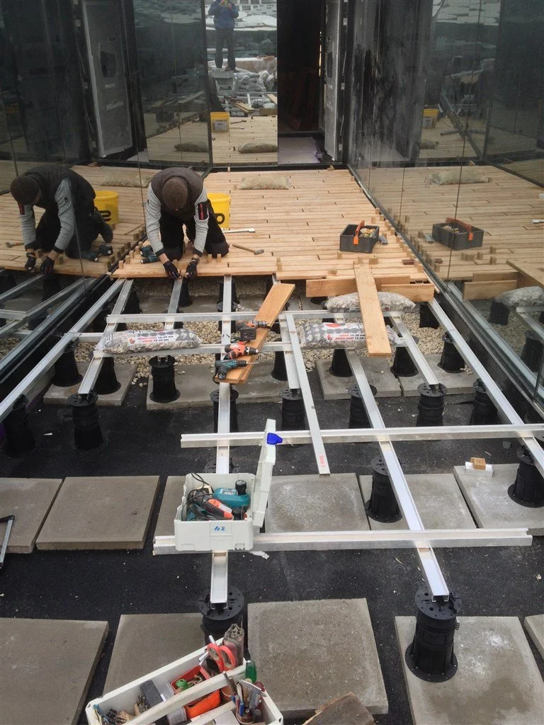 Zwei Handwerker bei der Verlegung eines hochwertigen Holzdecks auf einer modernen Stelzlager-Unterkonstruktion.