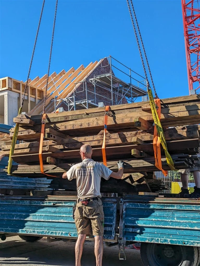 Zimmerer bei der Entladung von massiven Holzbauteilen mit einem Baukran auf der Baustelle.