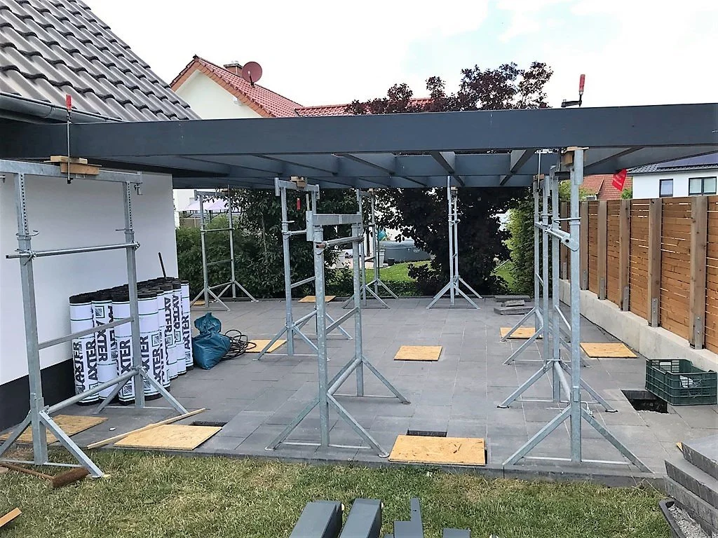 Hochwertiger Carport in Anthrazit mit integriertem Geräteraum; sichtbares Ständerwerk aus Leimbindern; Gerüstböcke im Vordergrund. hochwertig