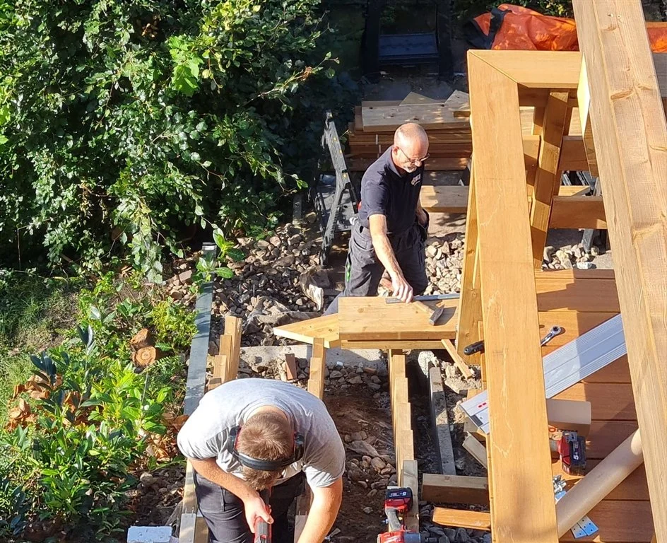 Zwei erfahrene Handwerker arbeiten gemeinsam an einer Holzkonstruktion für eine Terrasse.