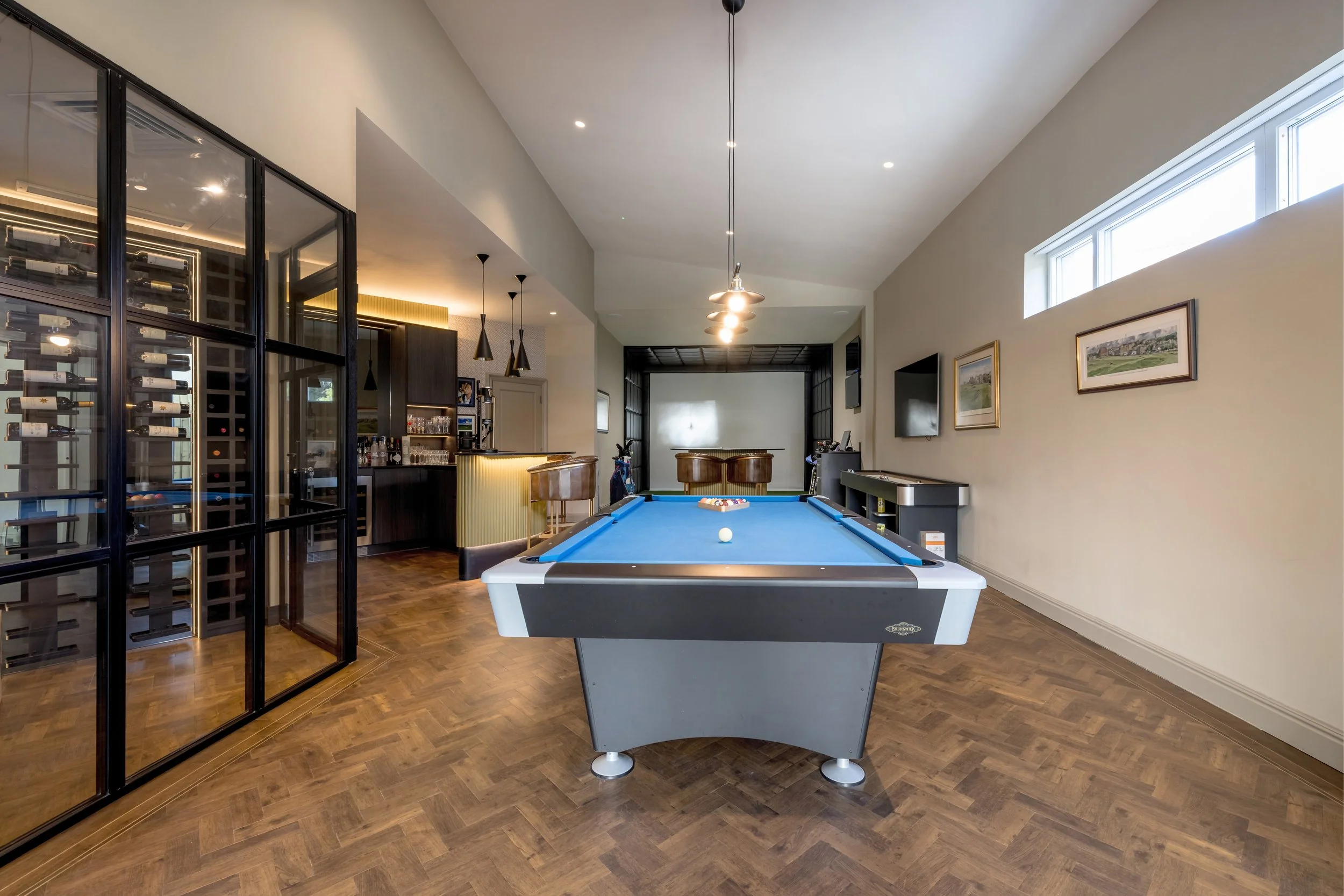 Indoor game room with pool table, bar area, and wine storage, illuminated by ceiling lights and natural light from window.