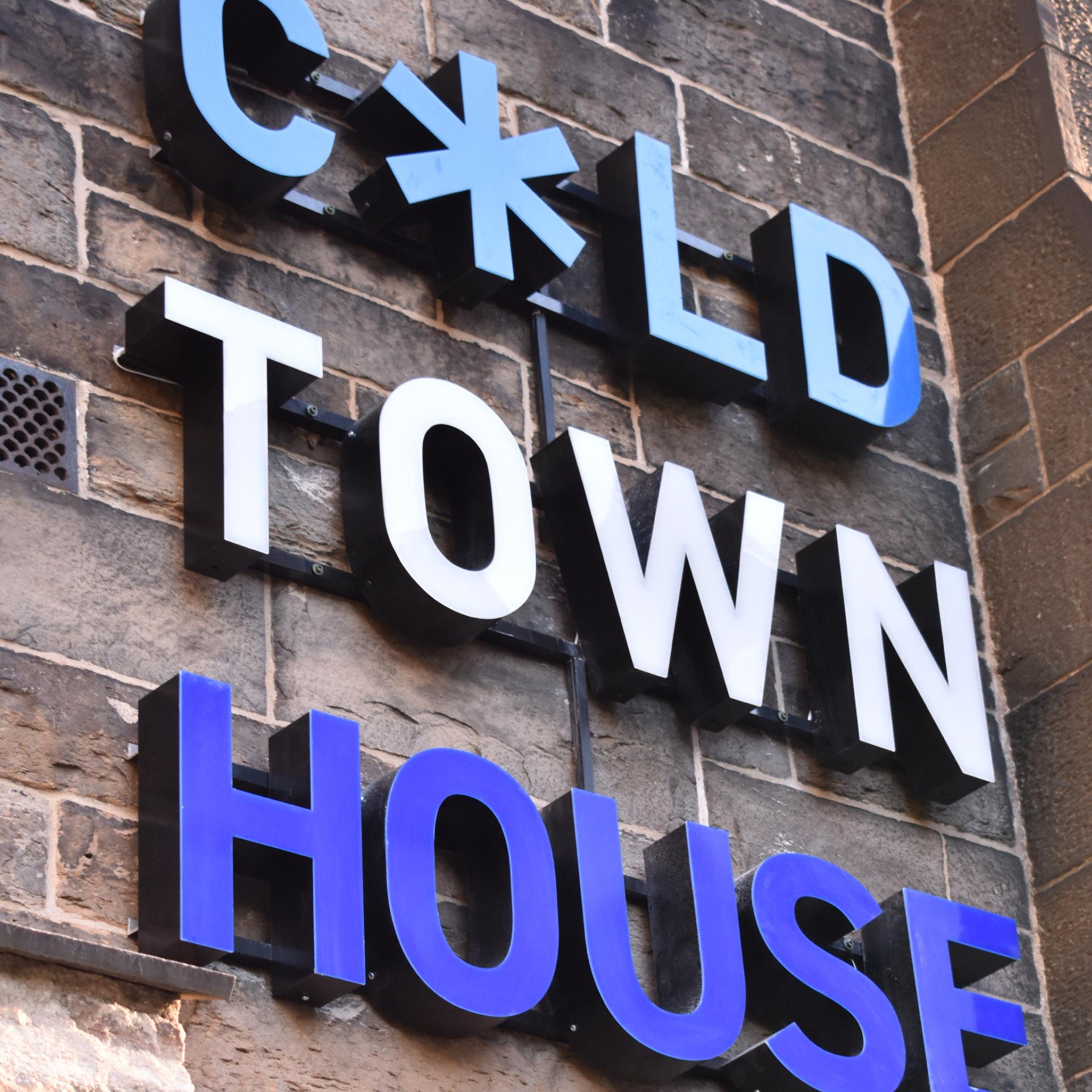Sign on brick wall reading 'COLD TOWN HOUSE' with glowing blue and white letters and a snowflake symbol.
