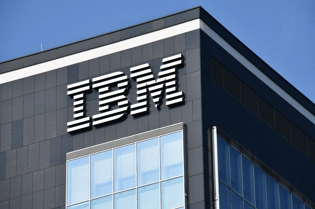 The IBM logo on the exterior of a modern office building with glass windows and a dark gray facade.
