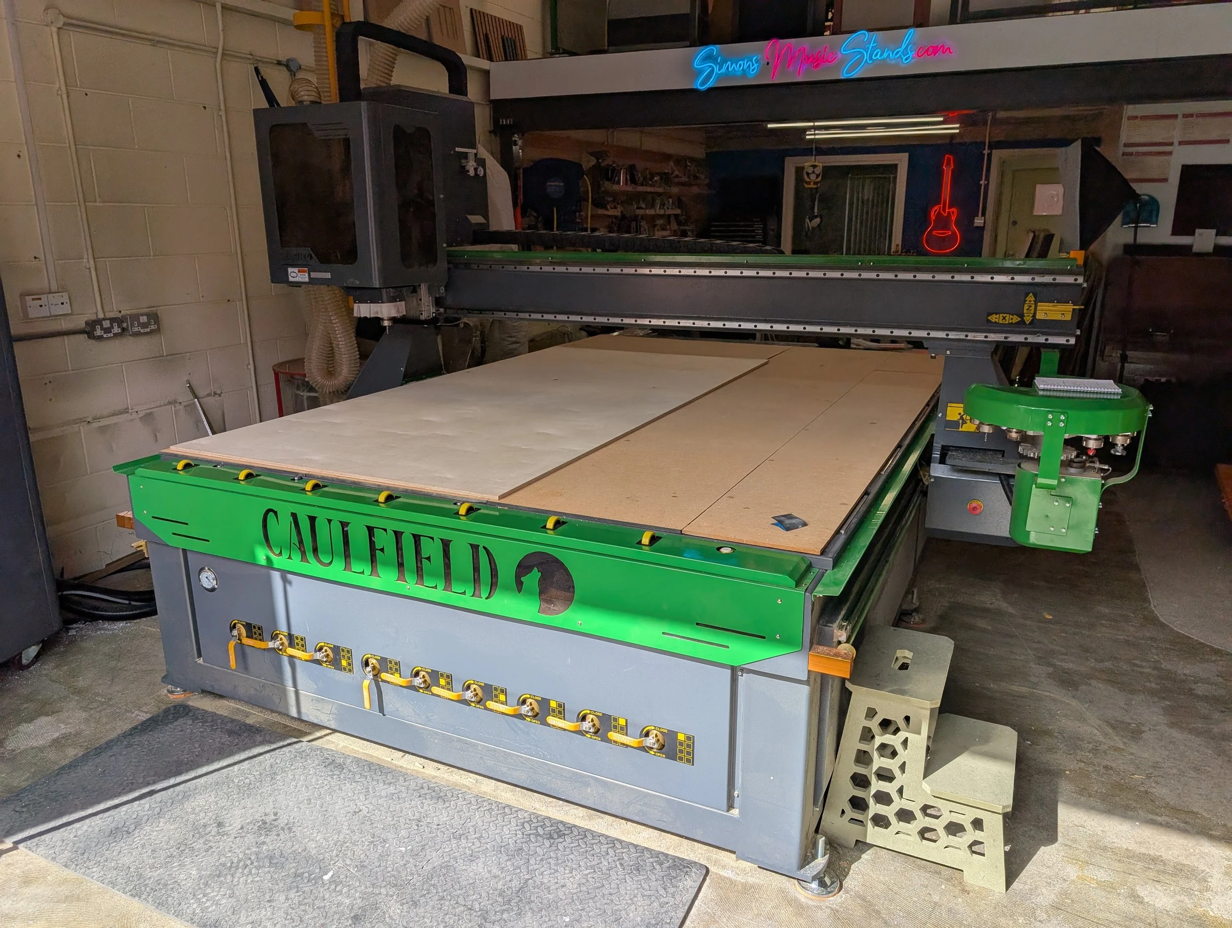 Large CNC Router cutter with a beige sheet material inside, situated in a workshop with a green front panel displaying the brand name 'Caulfield'.