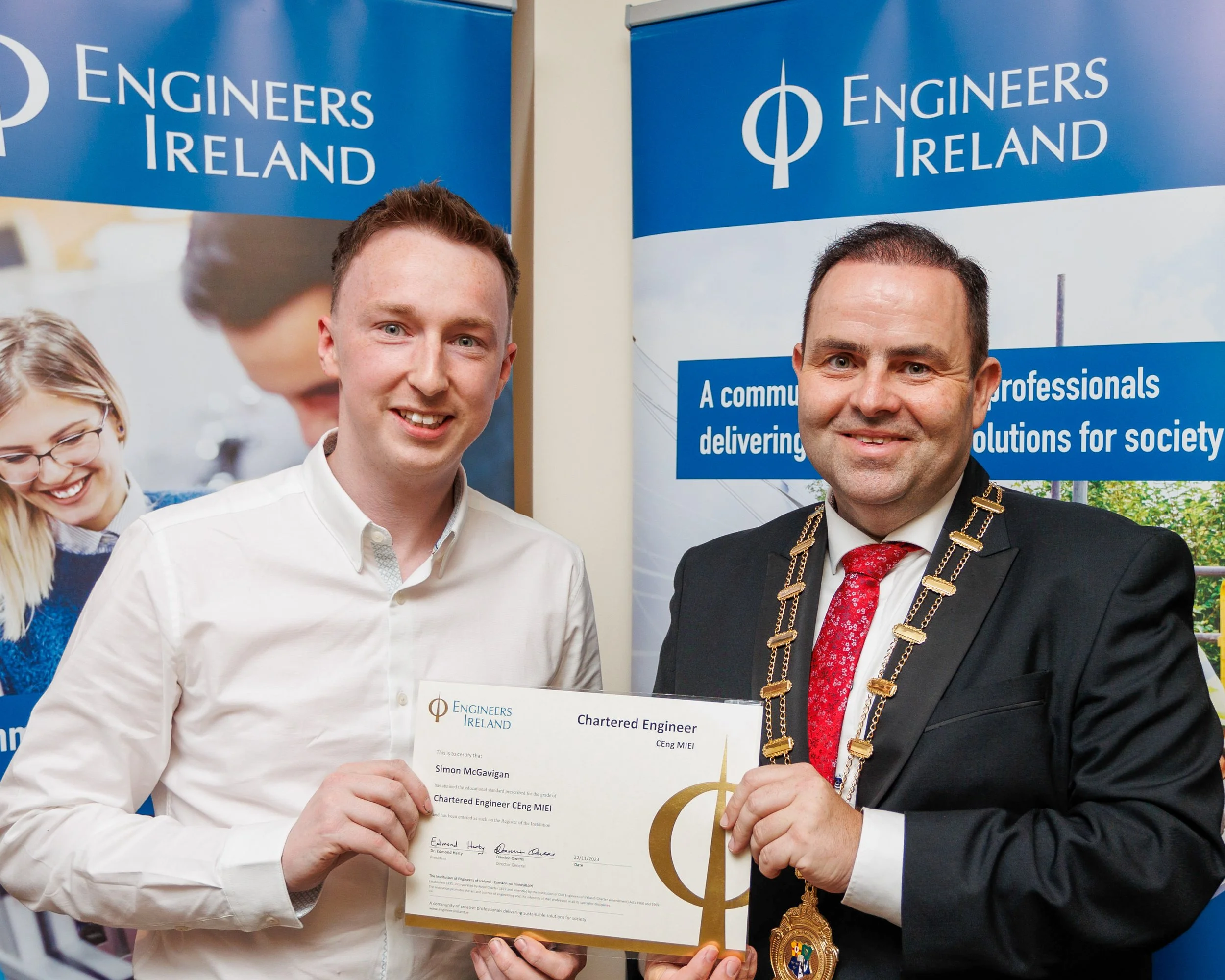 Two men smiling at a ceremony, one holding a Chartered Engineer certificate, standing in front of banners for Engineers Ireland.