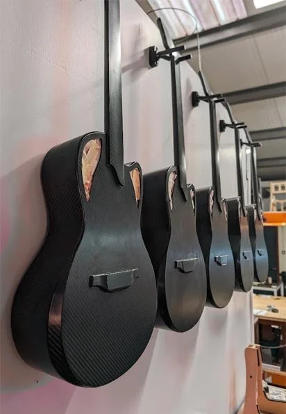 Several black electric guitars hanging on hooks on a wall in a workshop or music studio.