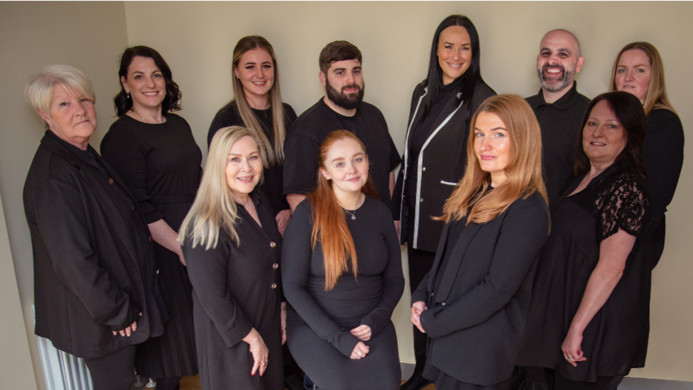 Group of 11 diverse people, mostly women, standing together in an indoor setting, posing for a photo.