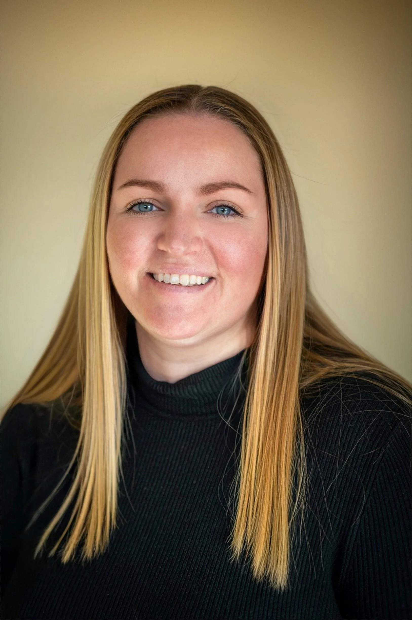 A young woman with blonde hair, blue eyes, and a black turtleneck smiling at the camera.