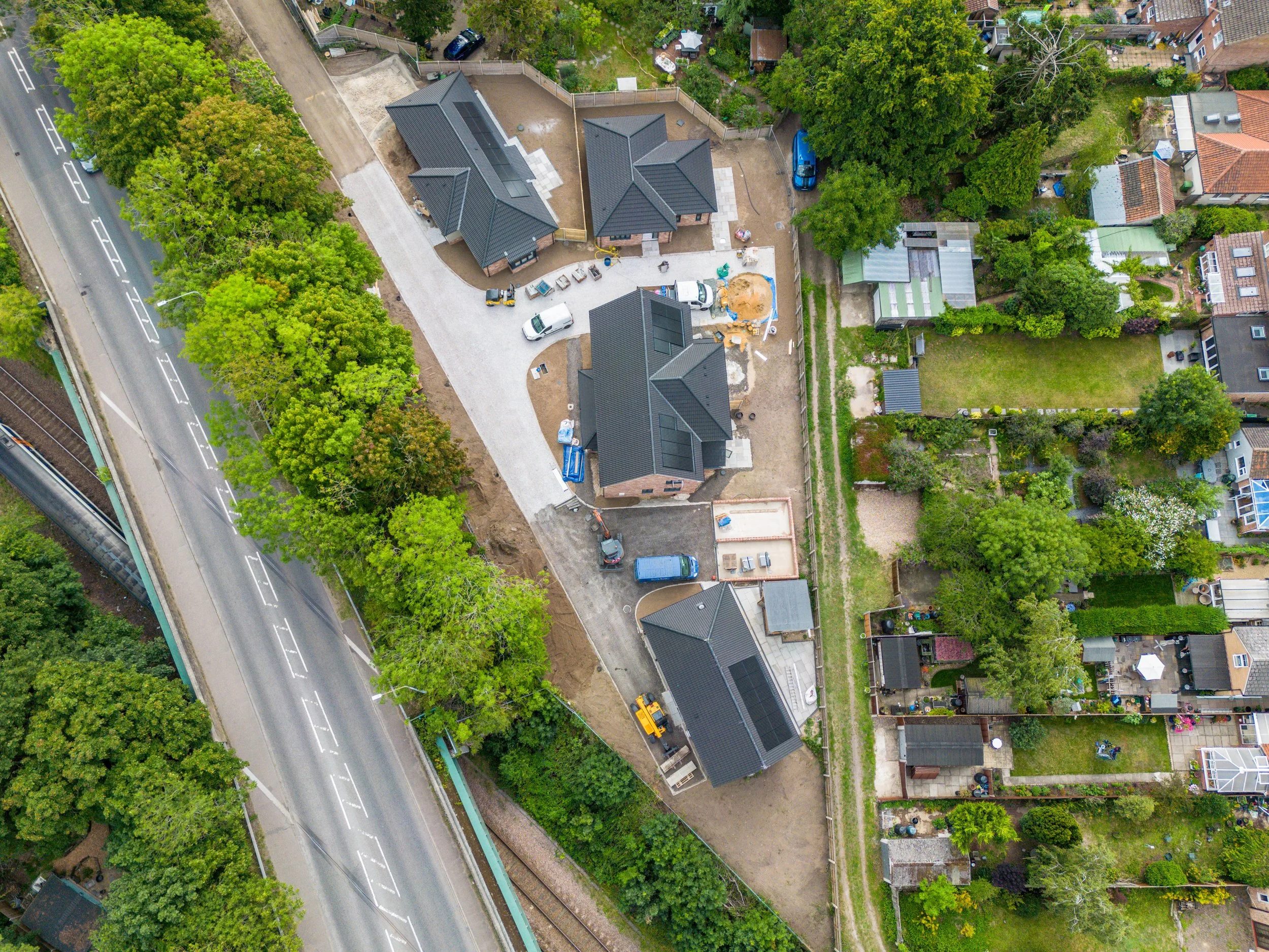  aerial view of a residential neighborhood with several houses under construction, parked vehicles, construction materials, and lush green trees along the streets and property boundaries.