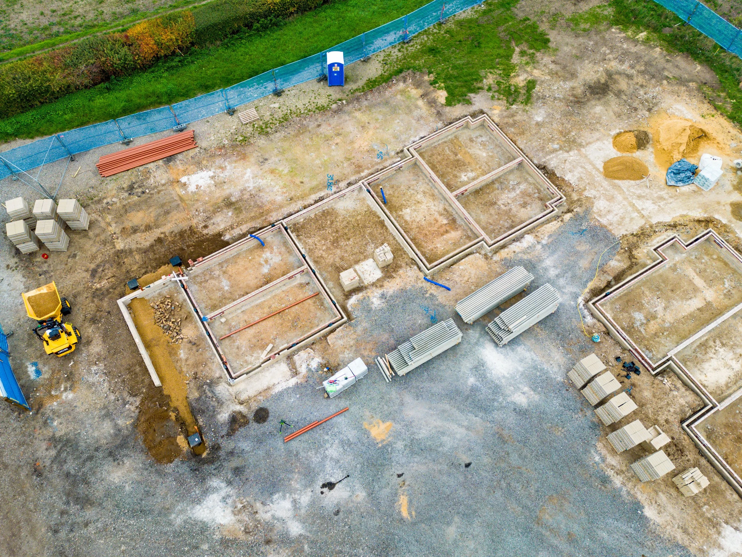 Aerial view of a construction site with partially built home foundations, construction materials, and equipment.
