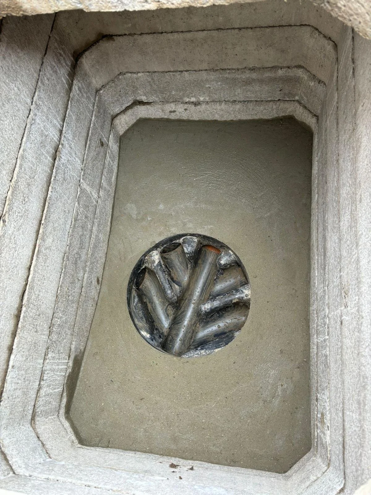 A circular metal grill with pipes inside, set into a concrete or stone surface with layered edging.