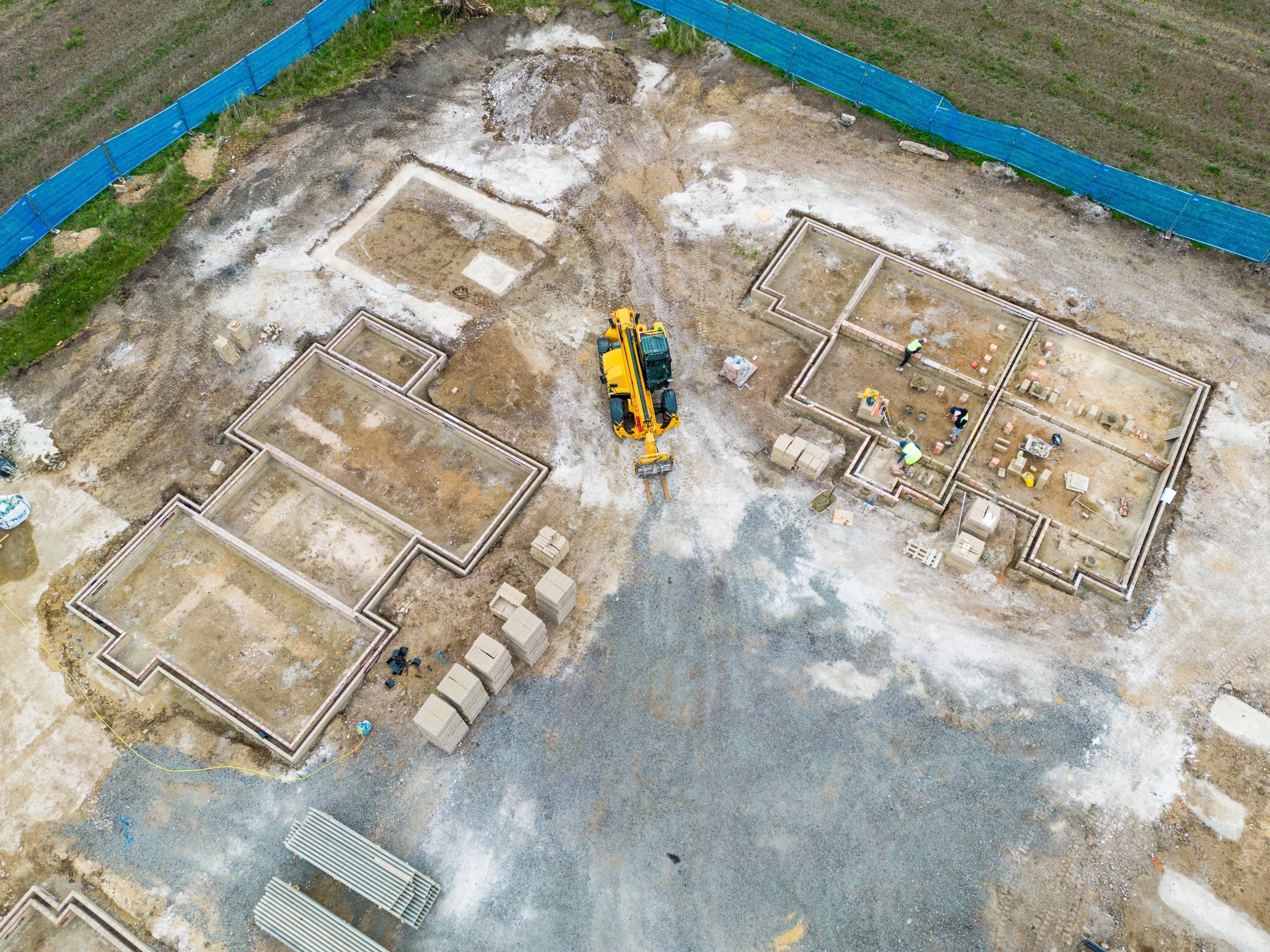 An aerial view of a construction site showing the foundations of multiple buildings with workers and construction equipment.