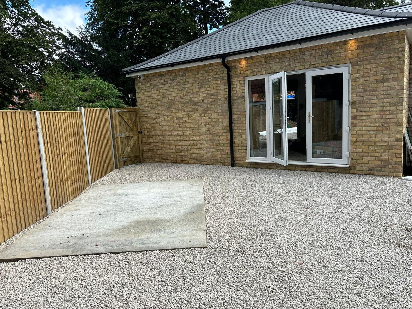 Backyard with gravel ground, a wooden fence, and a brick house with a folding glass door.