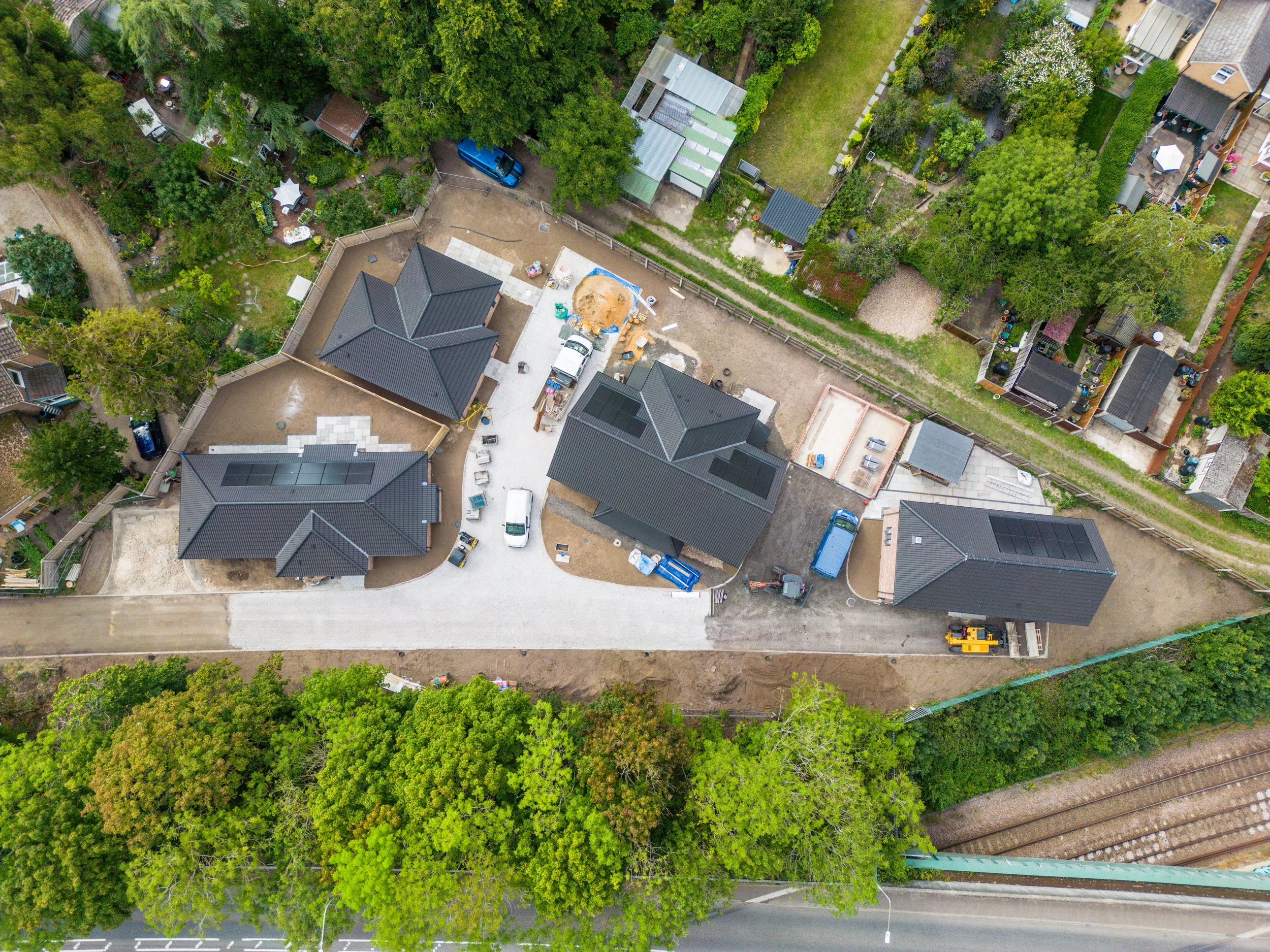 Aerial view of a residential area under construction with several buildings, cars, construction equipment, and surrounding trees.