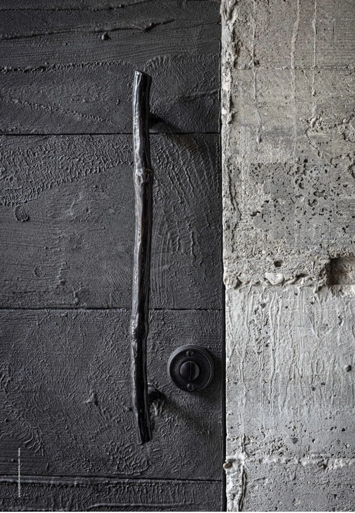 Close-up of a black door handle and lock on a dark wooden door next to a light-colored brick wall.