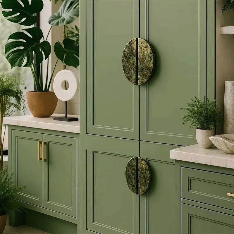 Green kitchen cupboards with marble handles, decorated with potted plants, a white sculpture, and a marble countertop.