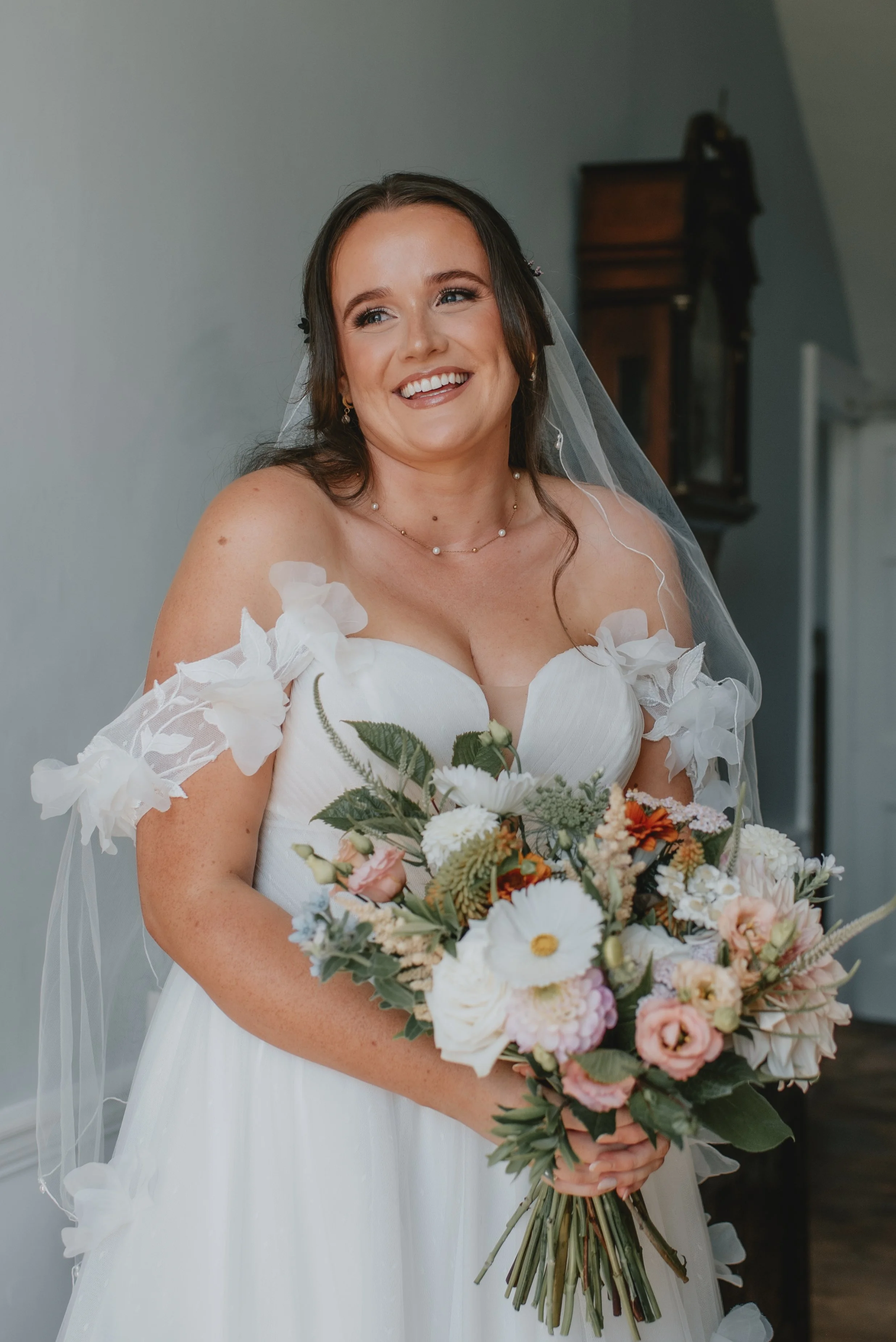 A smiling bride in a white wedding dress holding a bouquet of white and pastel flowers.