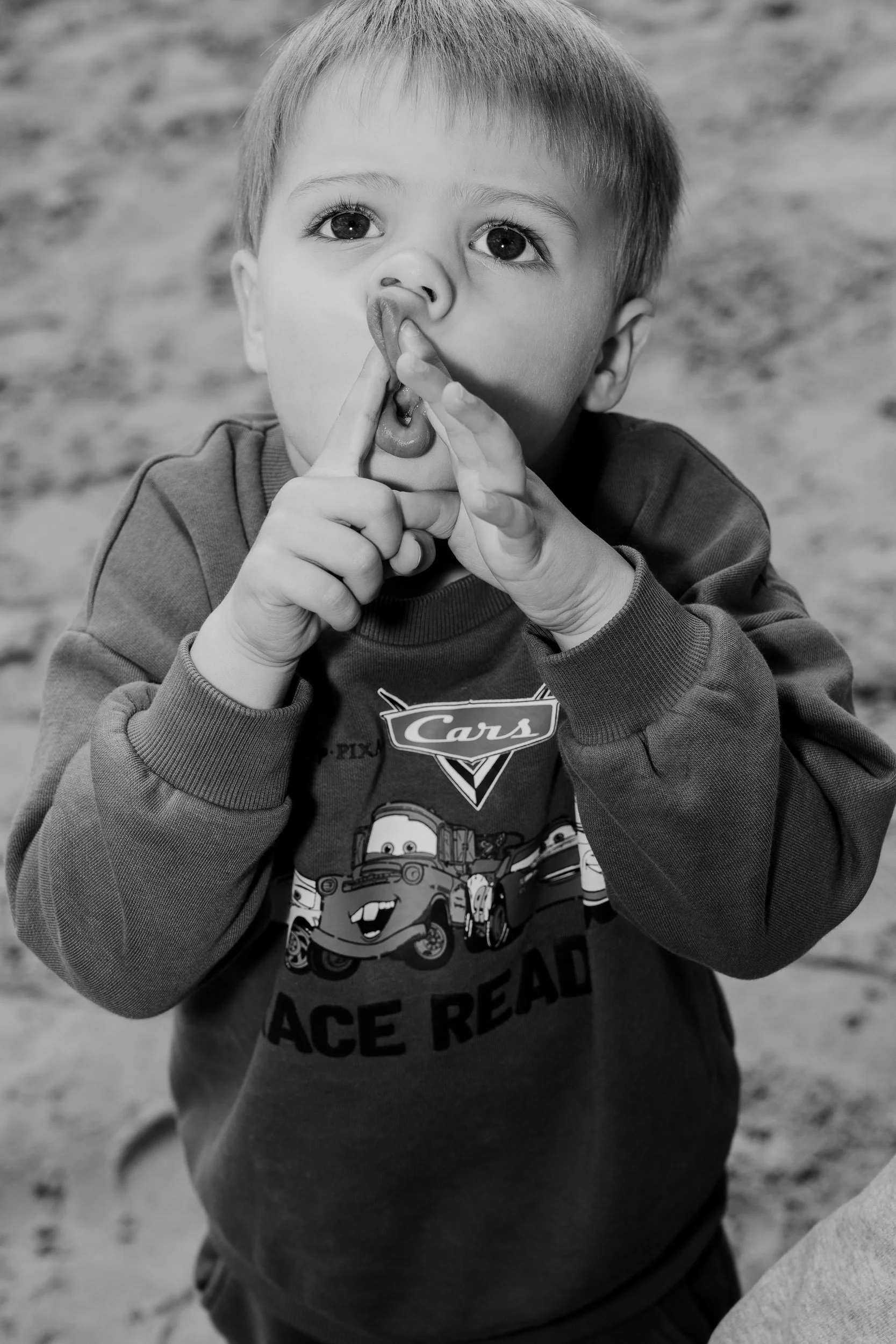 A young boy with light-colored hair and large eyes making a silly face with his finger in his nose and mouth.