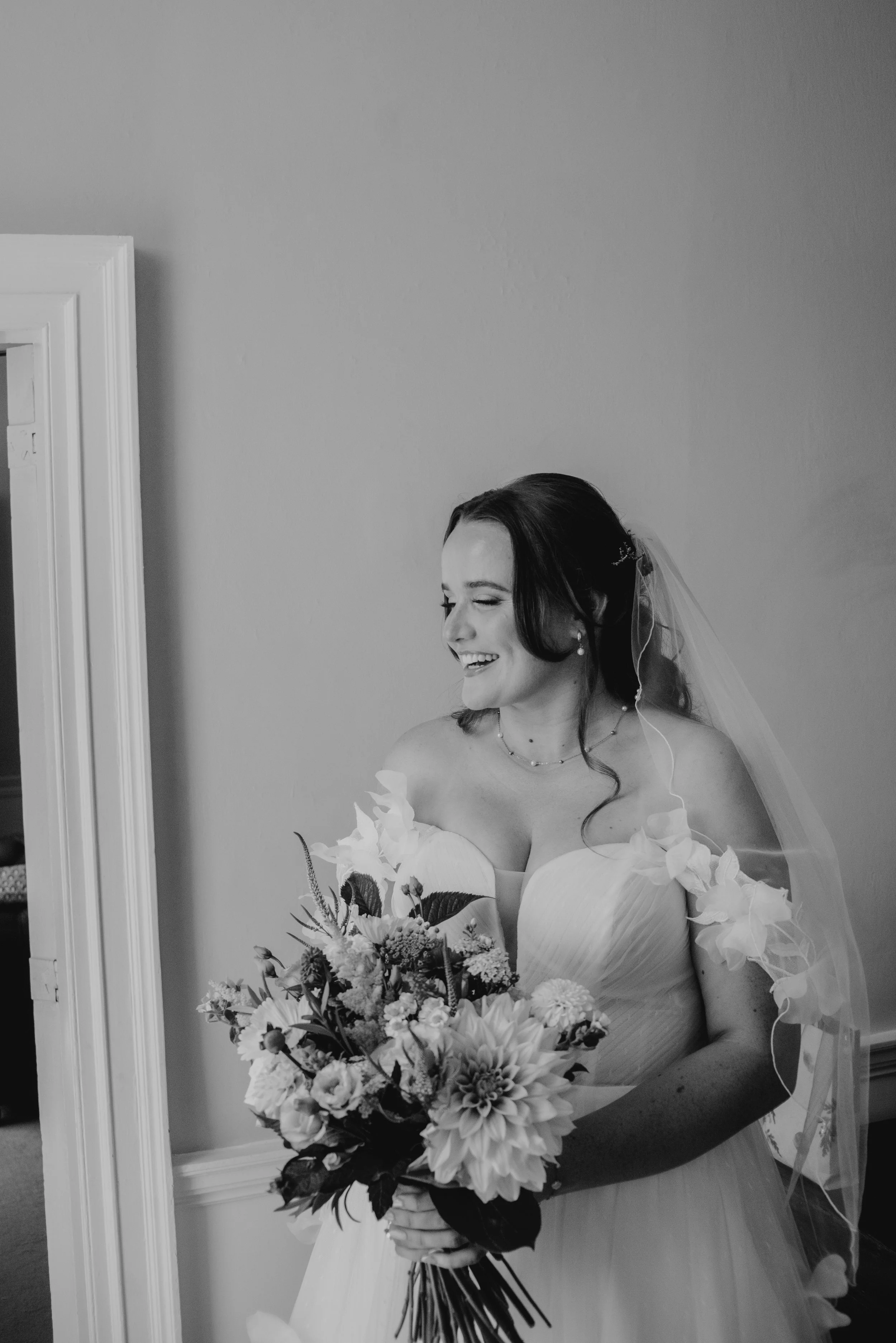 A newlywed couple sharing a joyful moment outdoors with sunlight in the background, wrapped in a sheer white veil.