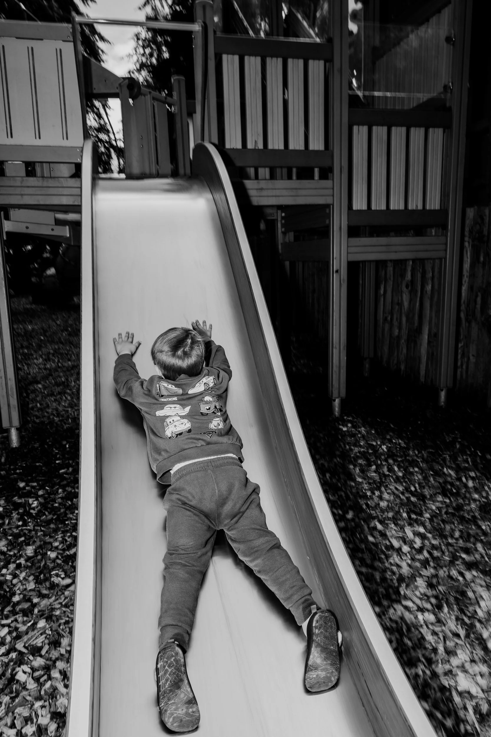Child sliding down outdoor playground slide with wooden fences and fallen leaves on ground