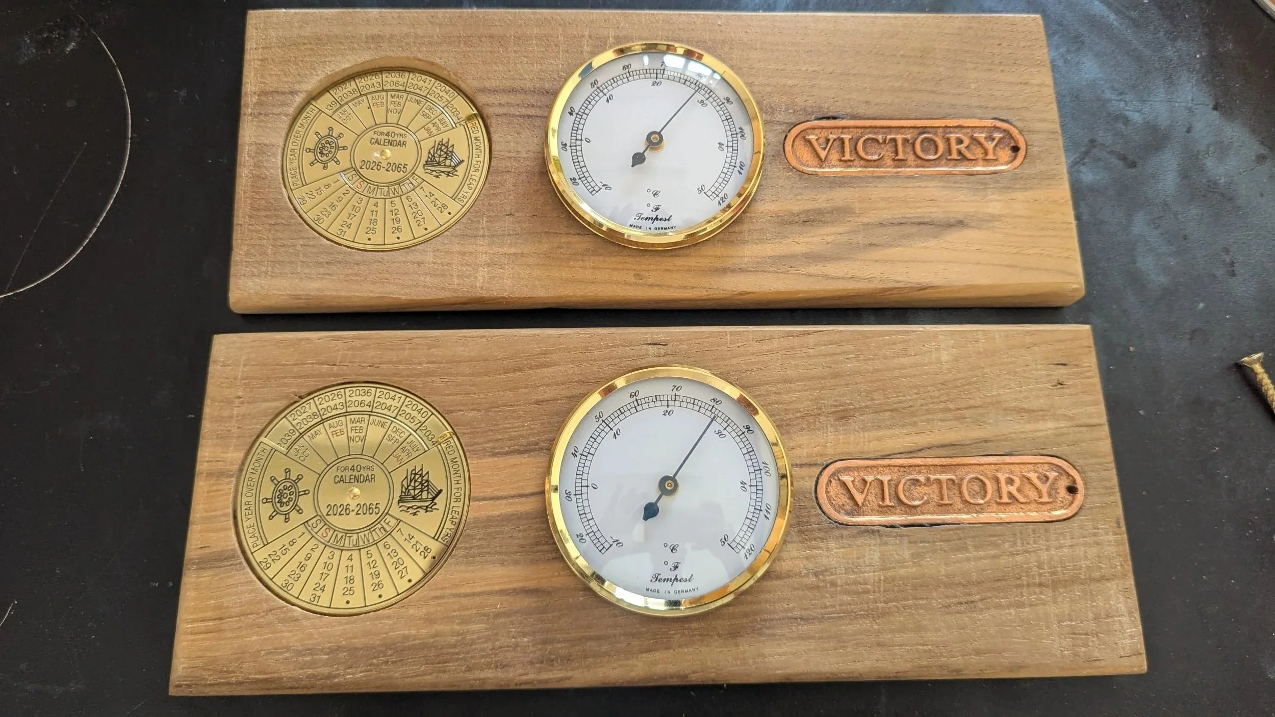 Two wooden boards with vintage-style weather instruments, each with a circular calendar, a thermometer, and a copper plaque that reads 'VICTORY'.