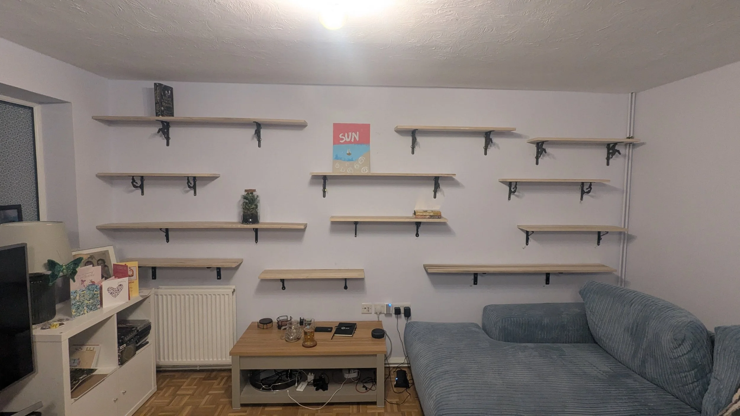 12 Shelves, filling a front room. Each shelf made from Tulip-wood, plain, sanded, and cut to varying lengths to show case their book collection in a cozy new home.