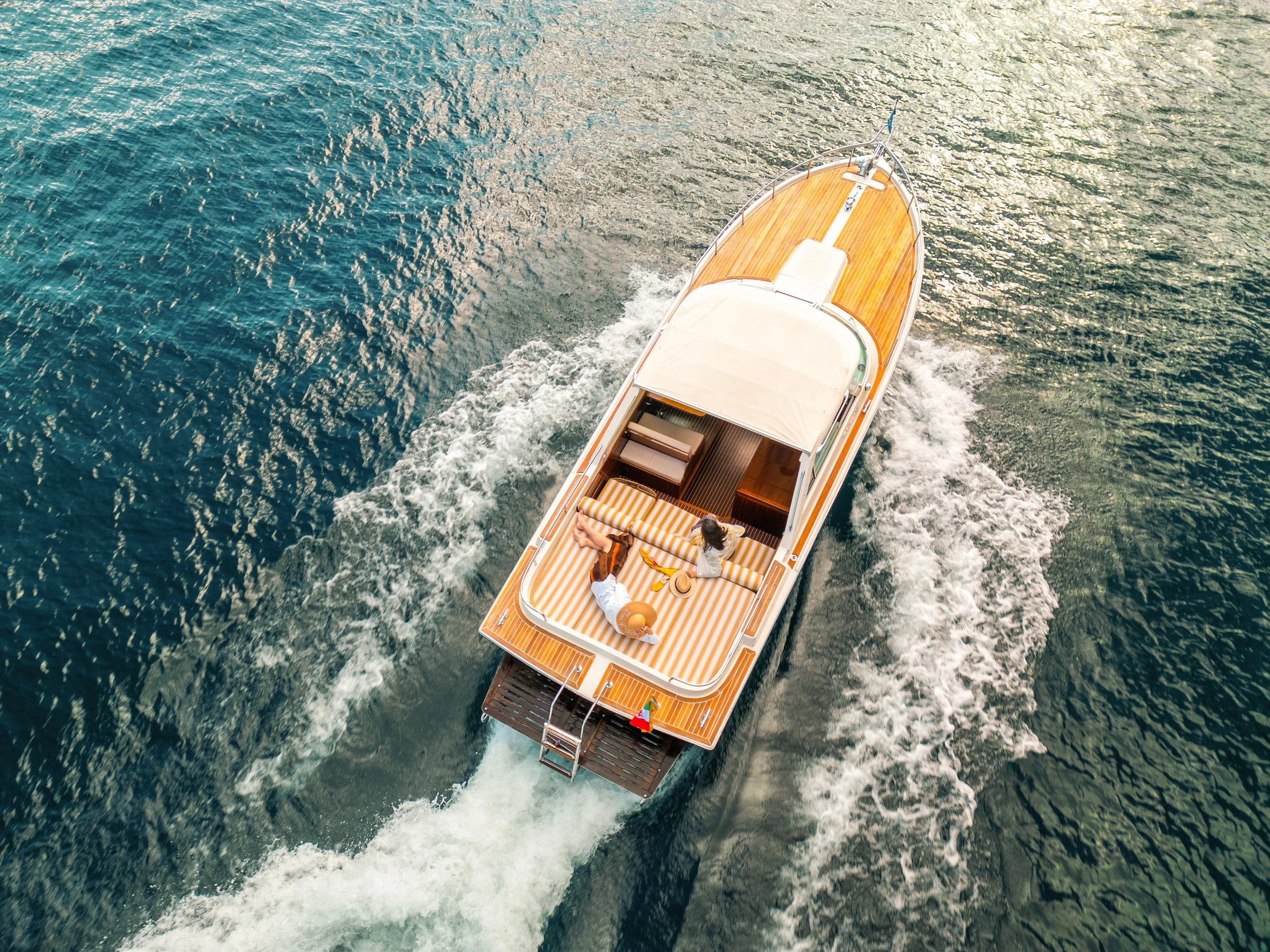 Aerial view of a boat cruising on the water with two people on the deck enjoying a sunny day.