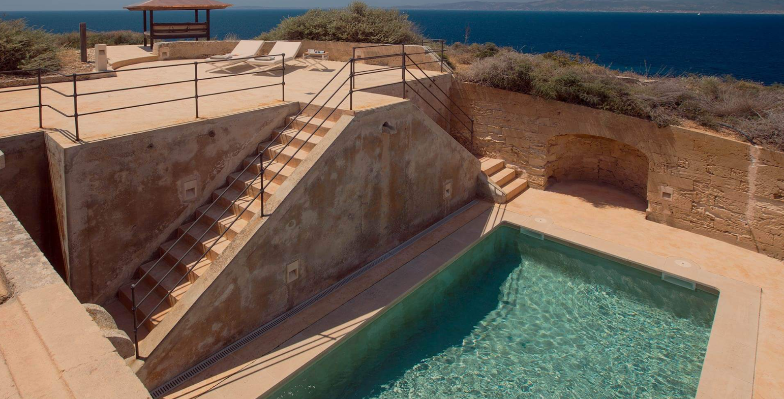 A pool area with stairs and a railing, overlooking the ocean, with a small shaded structure and two lounge chairs.