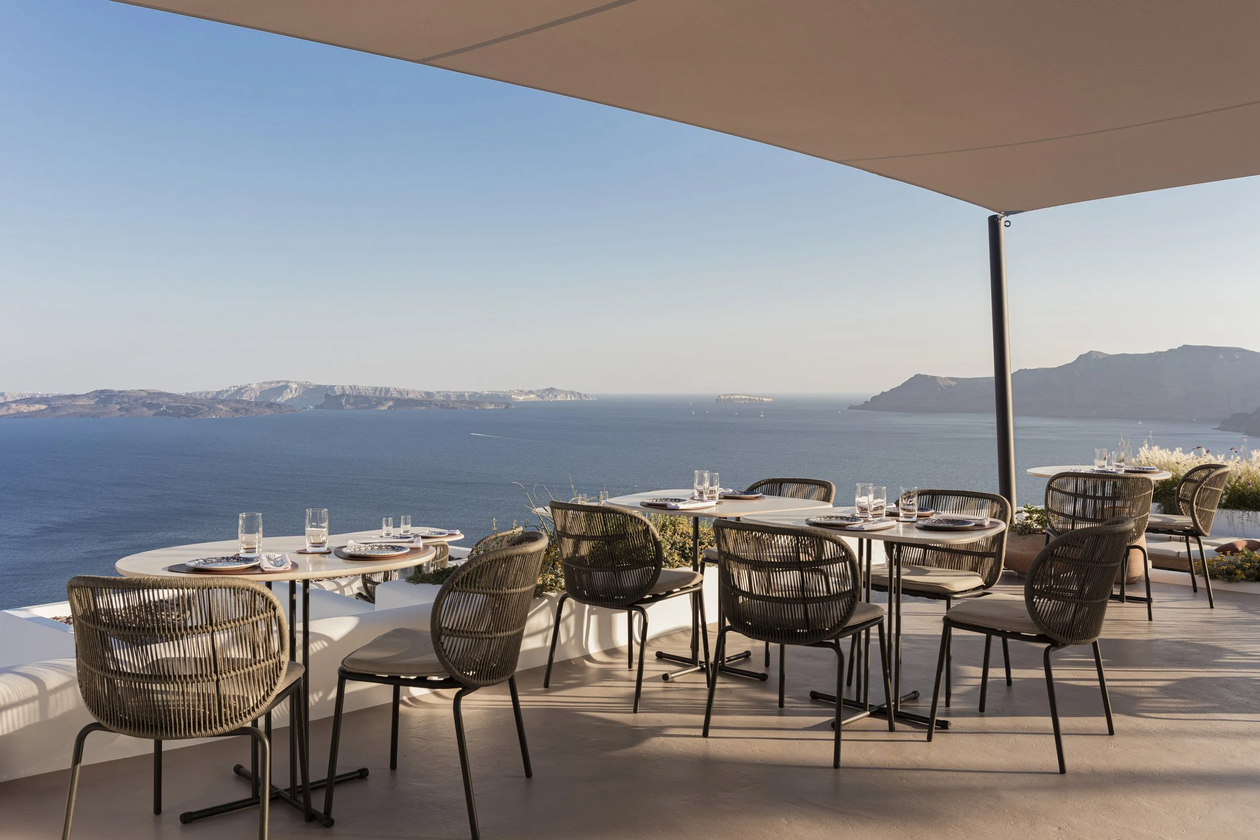 Outdoor restaurant with tables and chairs overlooking a body of water and distant land at sunset.