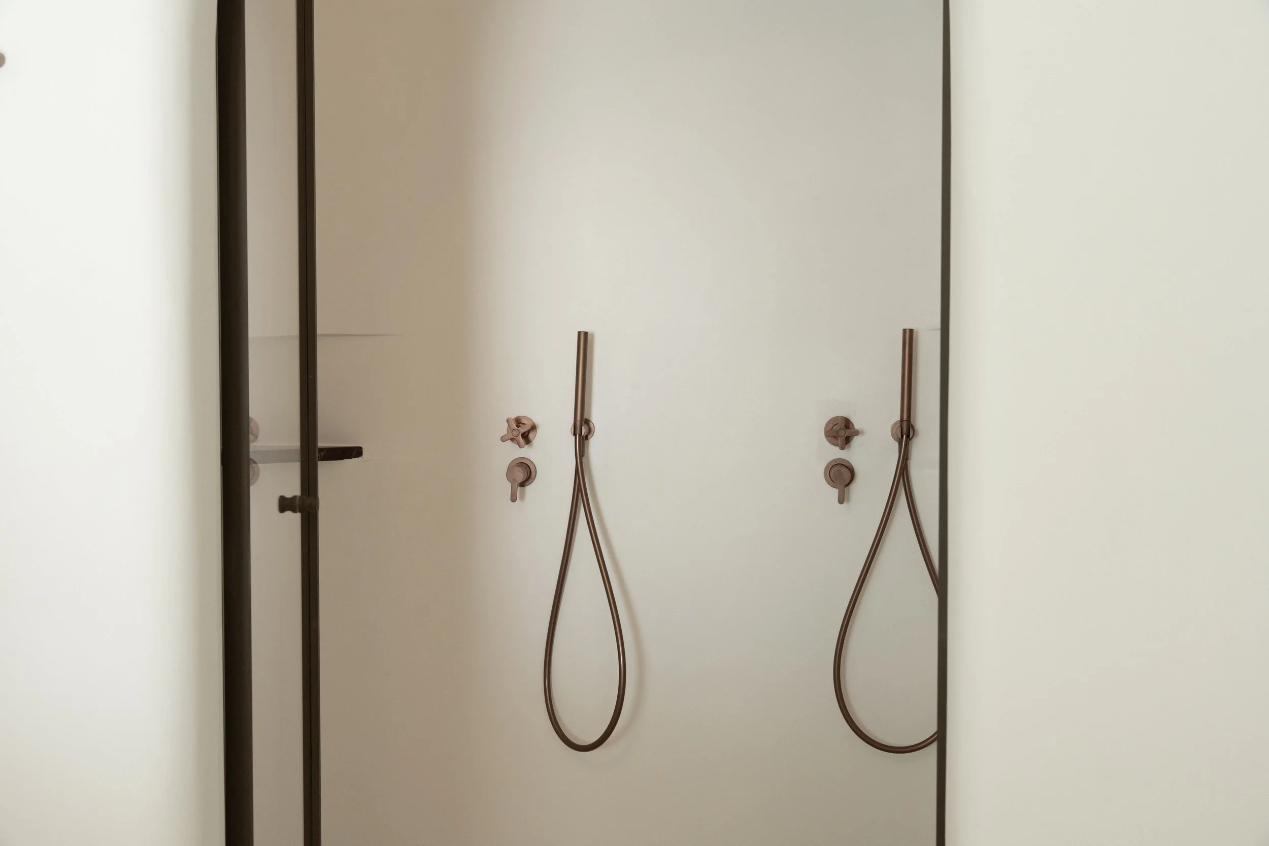 Shower area with two brown shower heads, two handles, and a shelf in the corner.