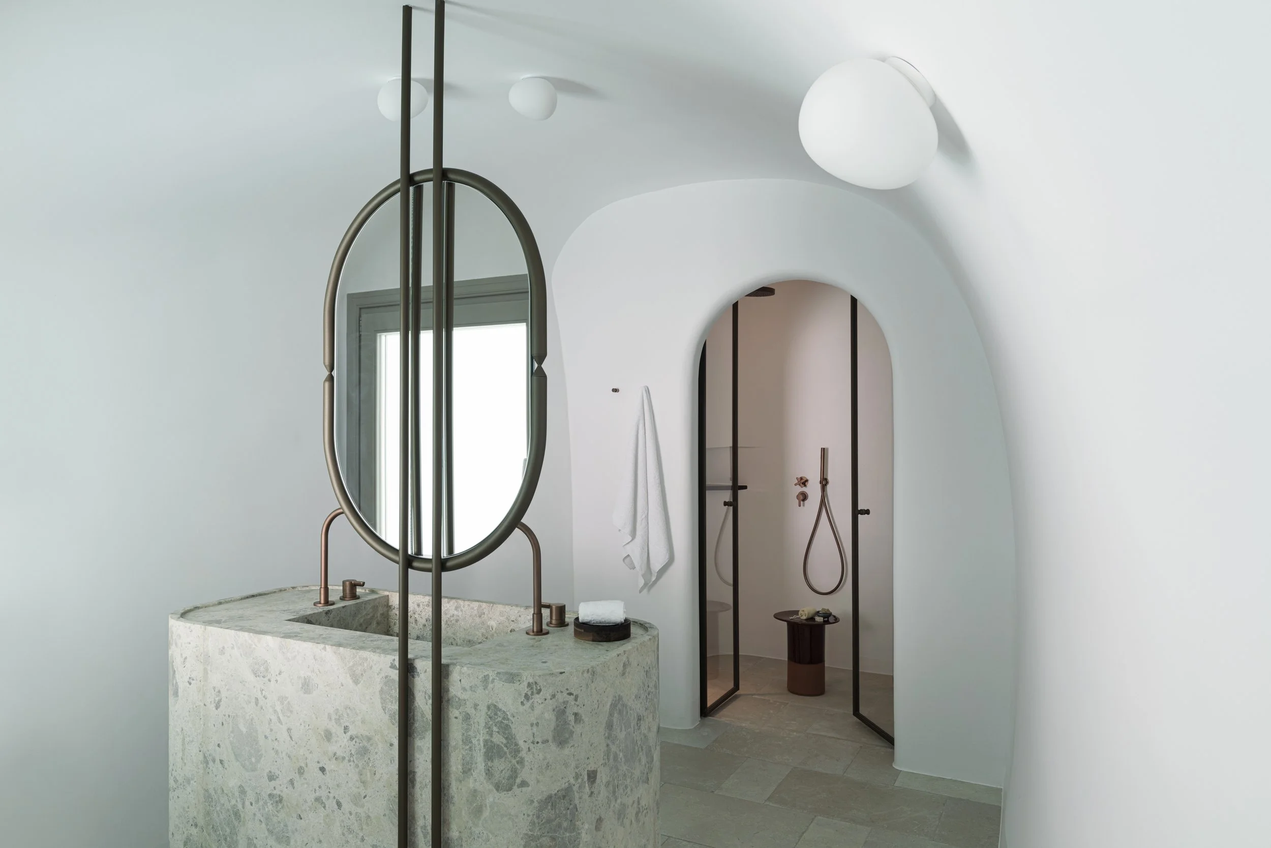 Minimalist bathroom with curved white walls, a stone sink with copper fixtures, and a glass shower enclosure with black trim.