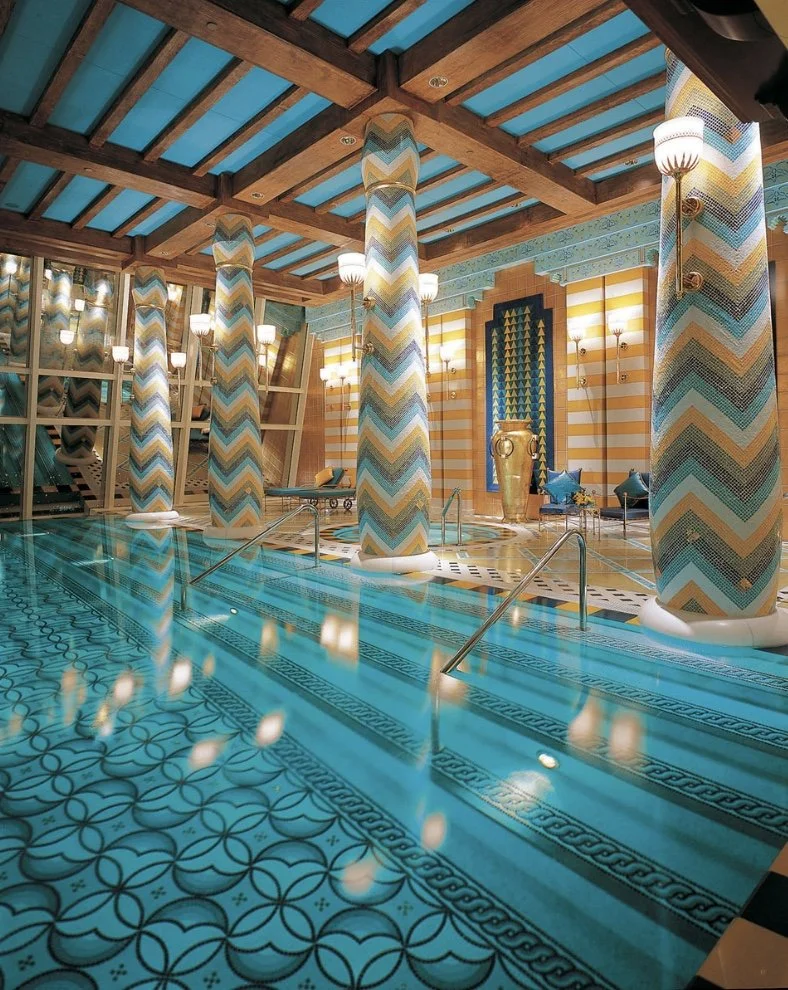 Indoor swimming pool with colorful chevron-patterned columns, warm lighting, and decorative tiles.