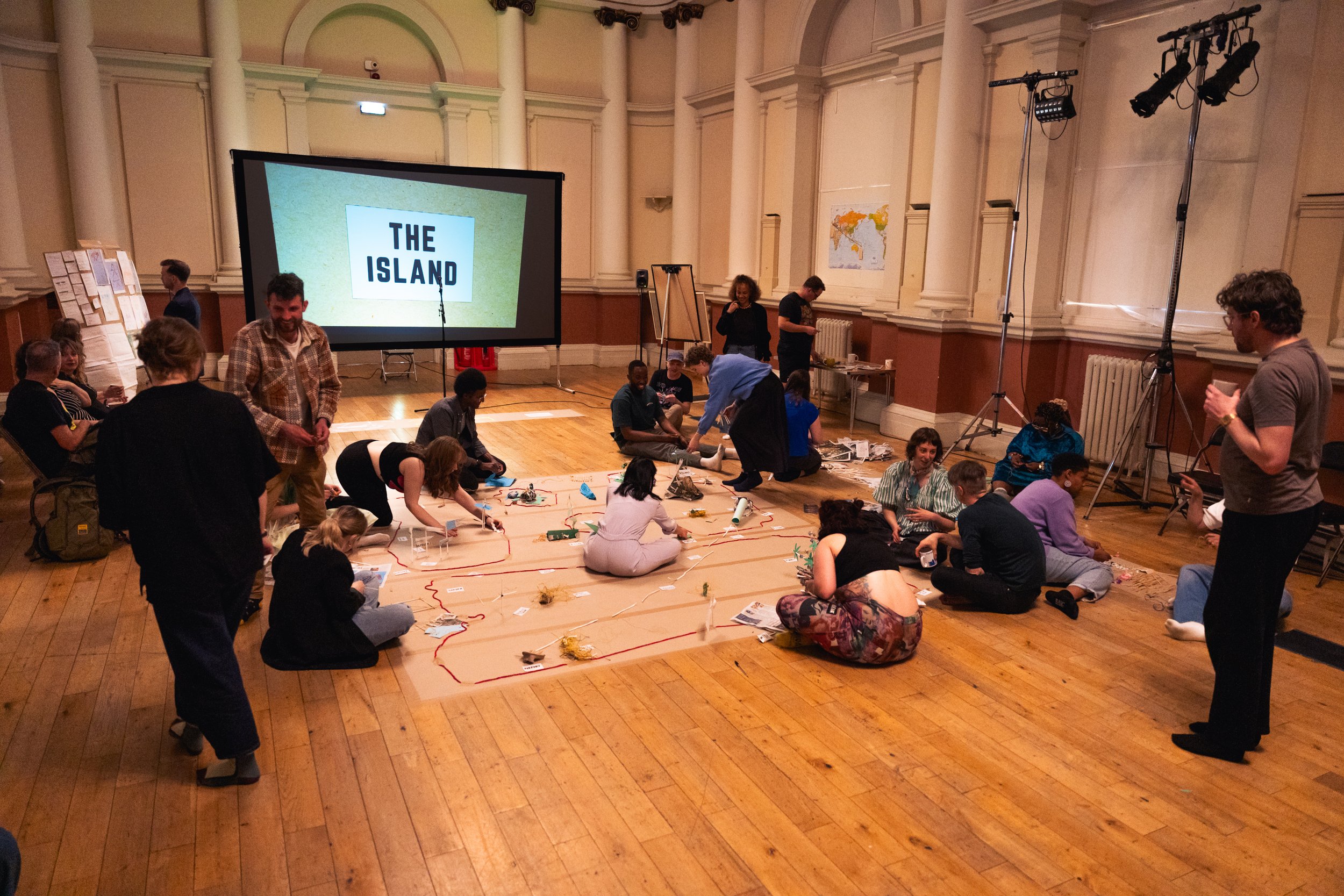 A group of adults sit around a large paper creating objects