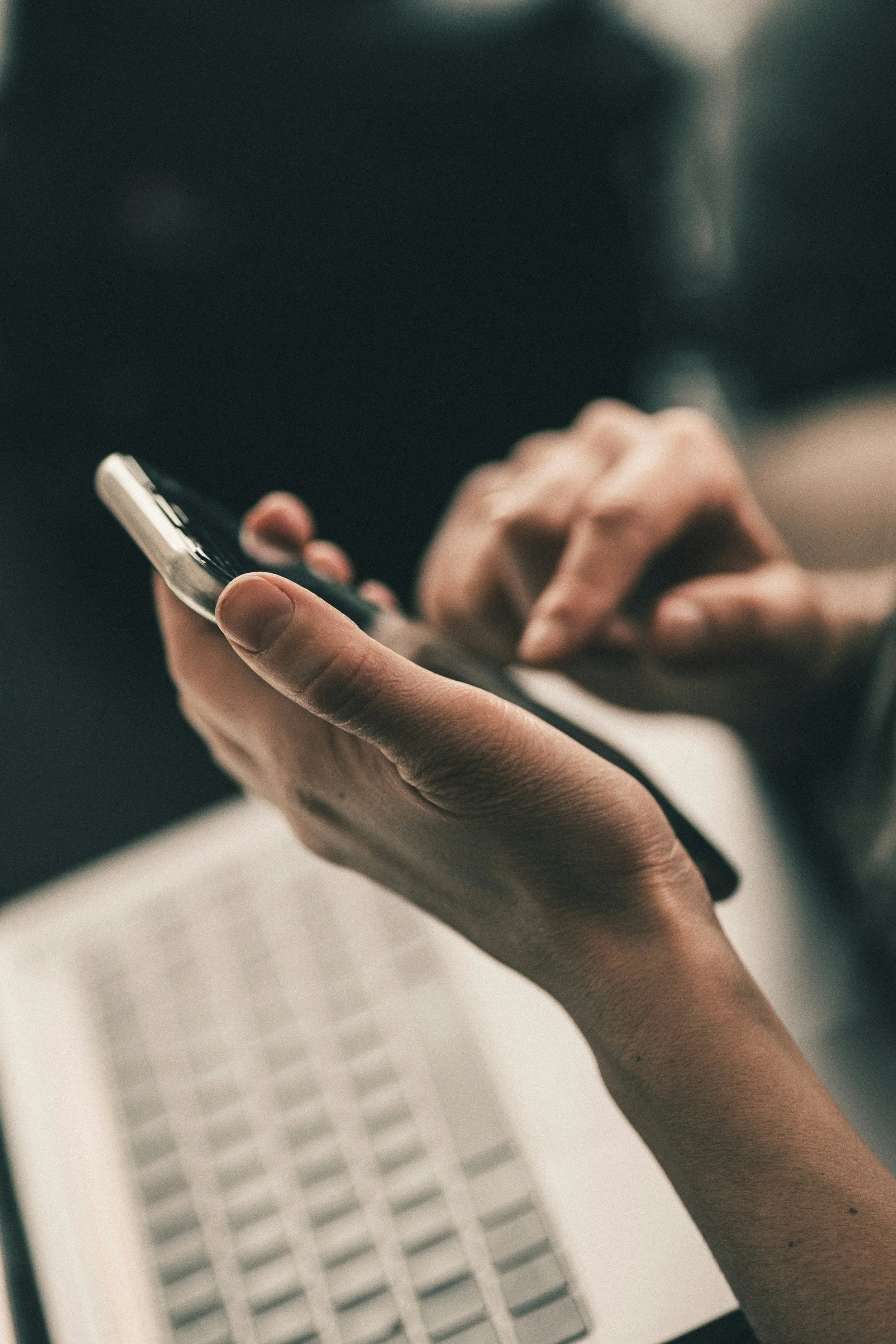 Manos sosteniendo un teléfono inteligente, con un teclado de computadora visible en el fondo.