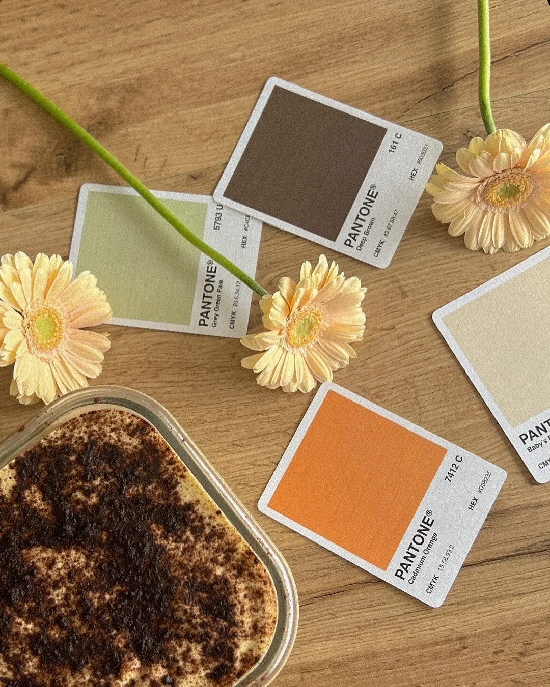 Pantone color swatches, beige flowers, and a dessert with cocoa on a wooden table.