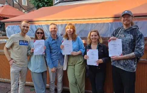 Group of Dutch students and their tutor holding completion certificates during an outdoor meet-up
