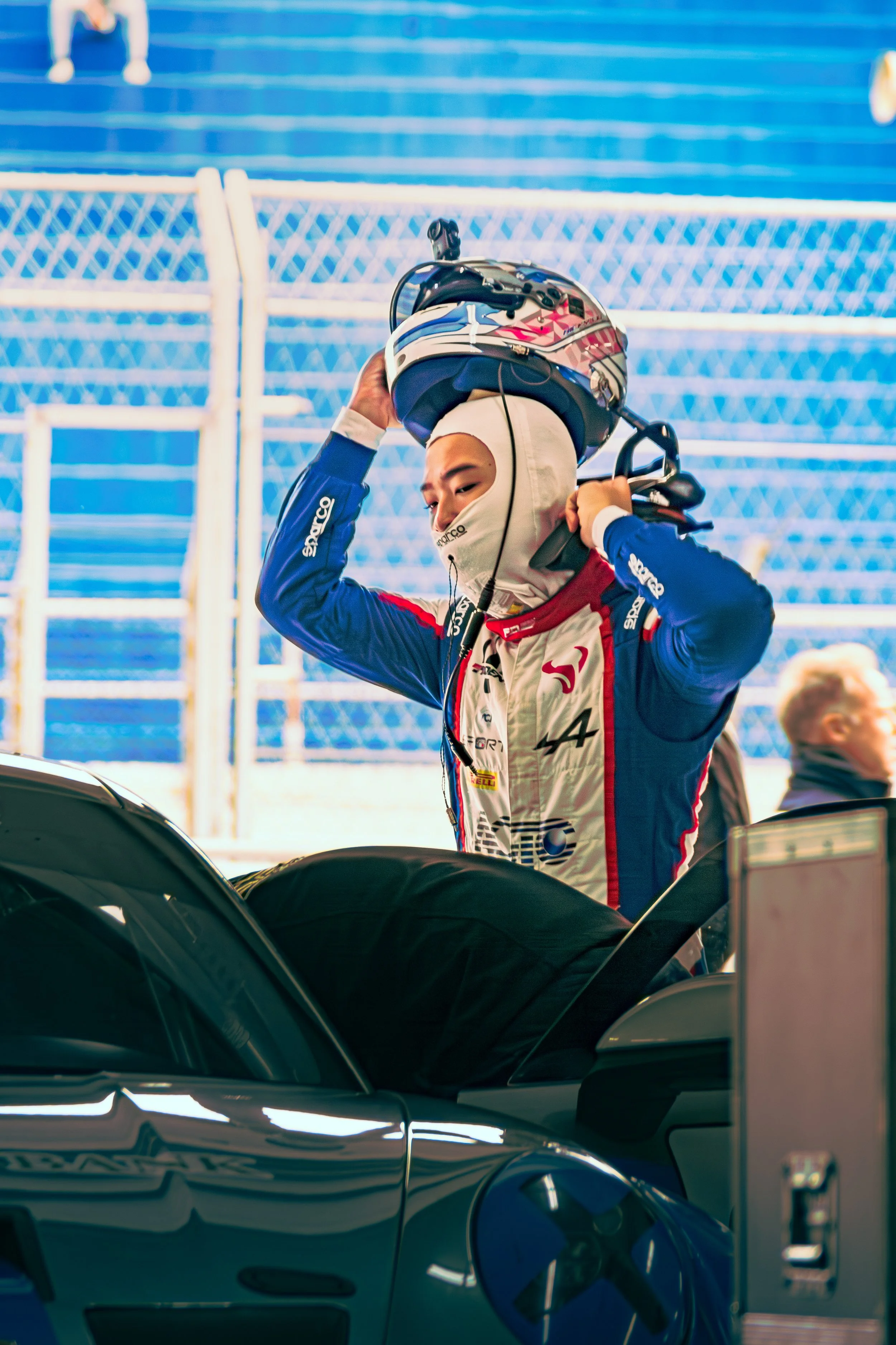 Race car driver in racing suit and helmet preparing to get into a car at a race track.