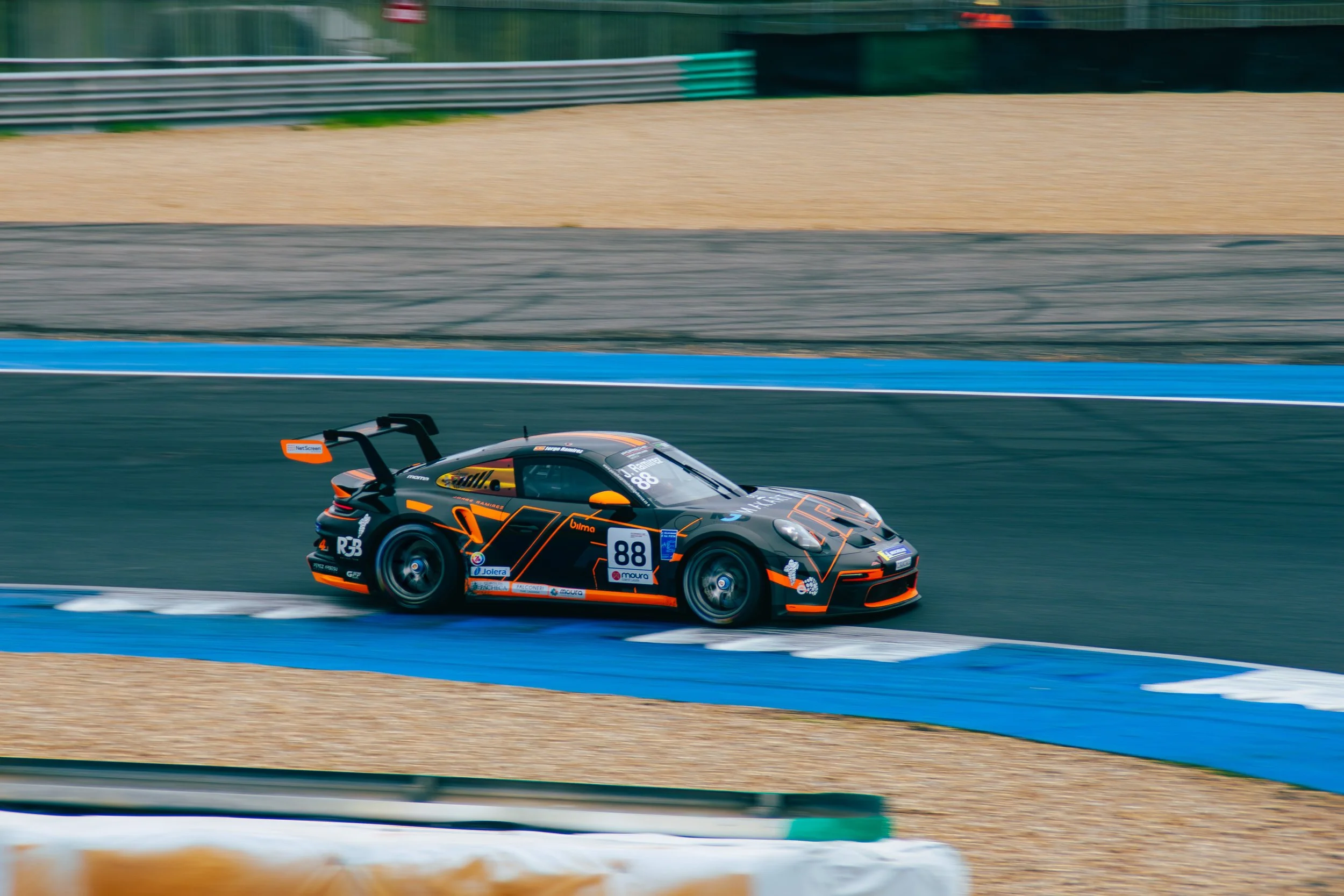 Race car on a race track moving at high speed, painted black with orange accents, number 88, with a large rear wing.