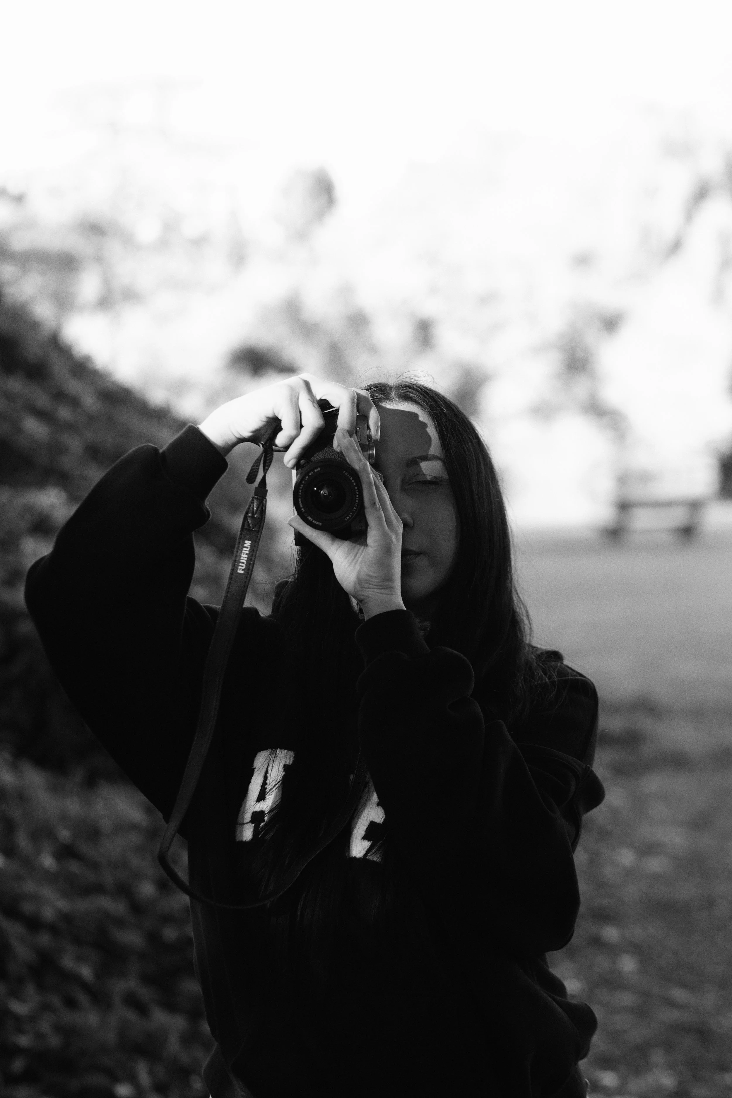 A woman taking a photo of herself in a mirror outdoors with a camera, black and white photograph.