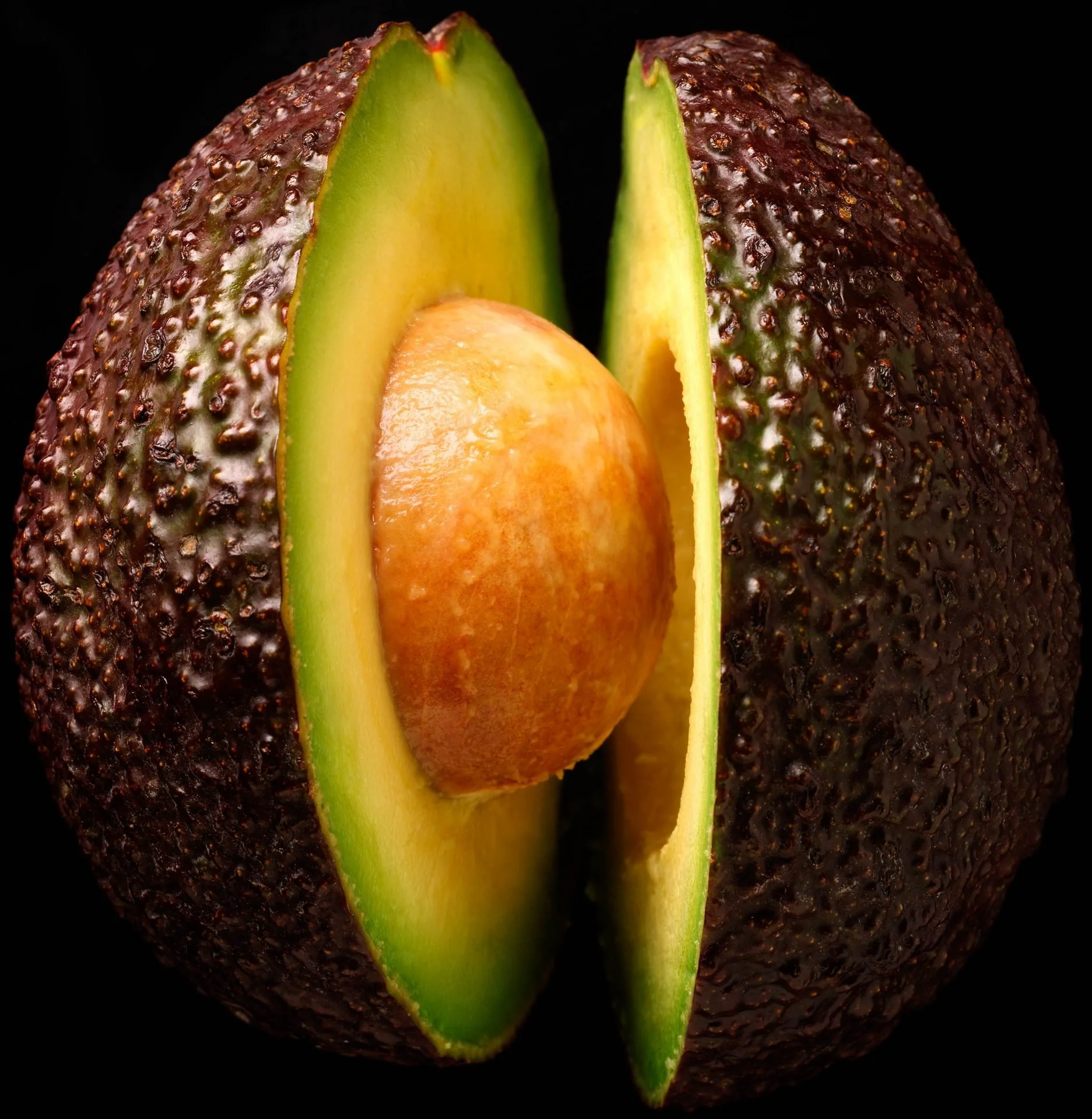 Close-up of a halved avocado with the seed still inside, against a black background.